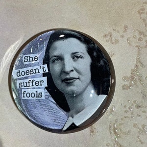 Puede incluir: Un objeto decorativo redondo de vidrio con una foto en blanco y negro de una mujer con el texto "She doesn't suffer fools" impreso en él.