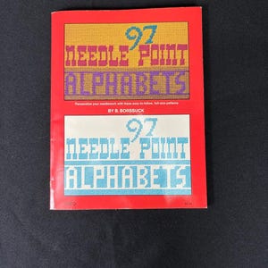May include: A red book titled "97 Needle Point Alphabets" with a yellow and purple design on the cover. The book includes patterns for needlepoint alphabets. The author's name is B. Borssuck.