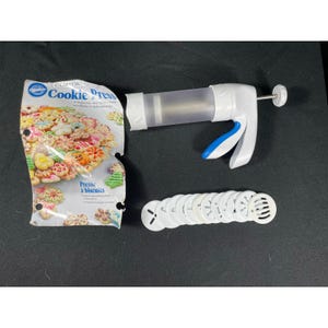 May include: A white and blue Comfort Cookie Press kit with a clear cylinder, a handle, and a set of 12 cookie disc shapes. The packaging shows colorful cookies. Includes 12 discs and recipe.