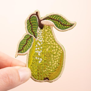 Op de afbeelding: Geborduurde patch in de vorm van een peer, in groen- en geeltinten. De peer heeft een textuur met witte accenten en wordt vergezeld door twee groene bladeren met bruine details.