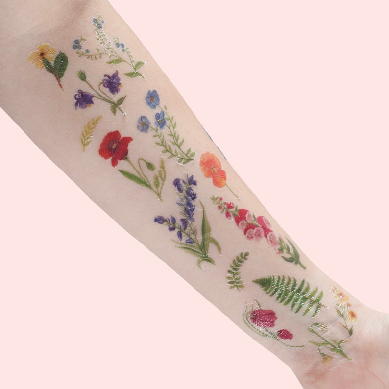 Puede incluir: Una hoja de tatuajes temporales con una variedad de flores y helechos coloridos. Los tatuajes est&aacute;n dise&ntilde;ados para parecer ilustraciones bot&aacute;nicas realistas.