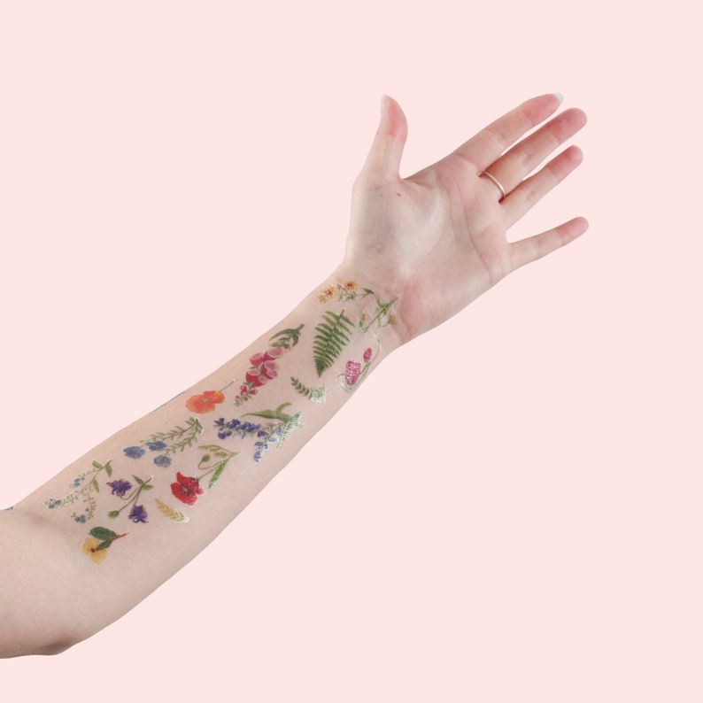 Puede incluir: Un brazo con varios tatuajes temporales de flores y hojas de colores.