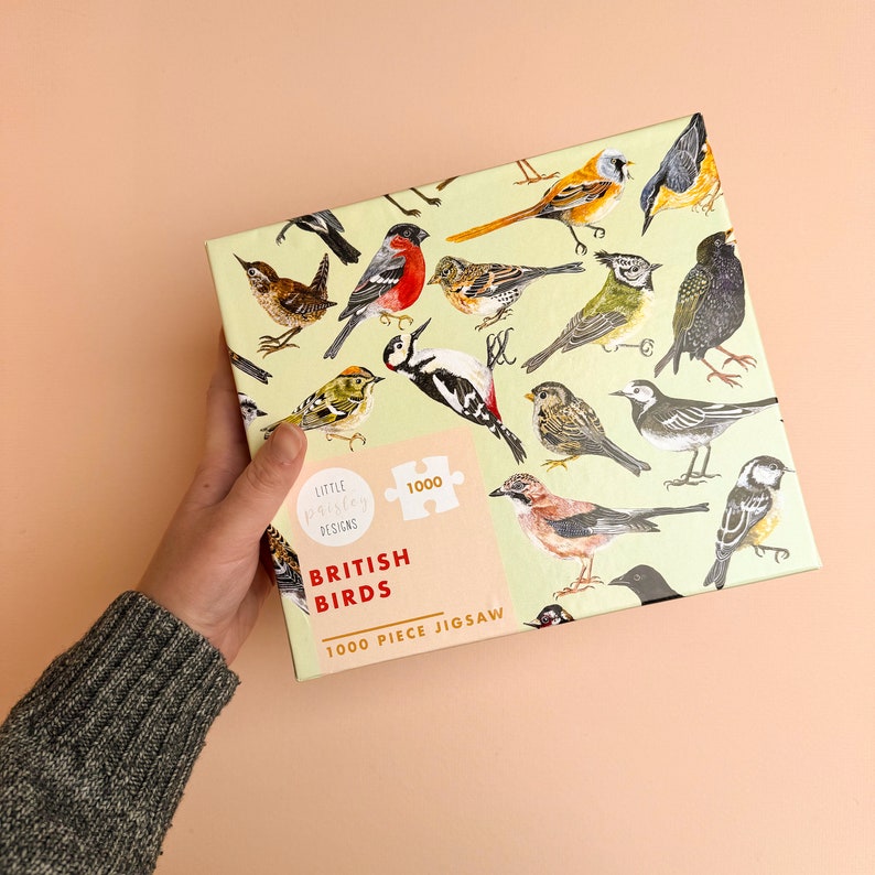 May include: A 1000 piece jigsaw puzzle featuring a variety of British birds on a light green background. The puzzle box has a light green background with a white border and the text "British Birds 1000 Piece Jigsaw" in red and black lettering. The puzzle box also features a small logo for "Little Pixel Designs".