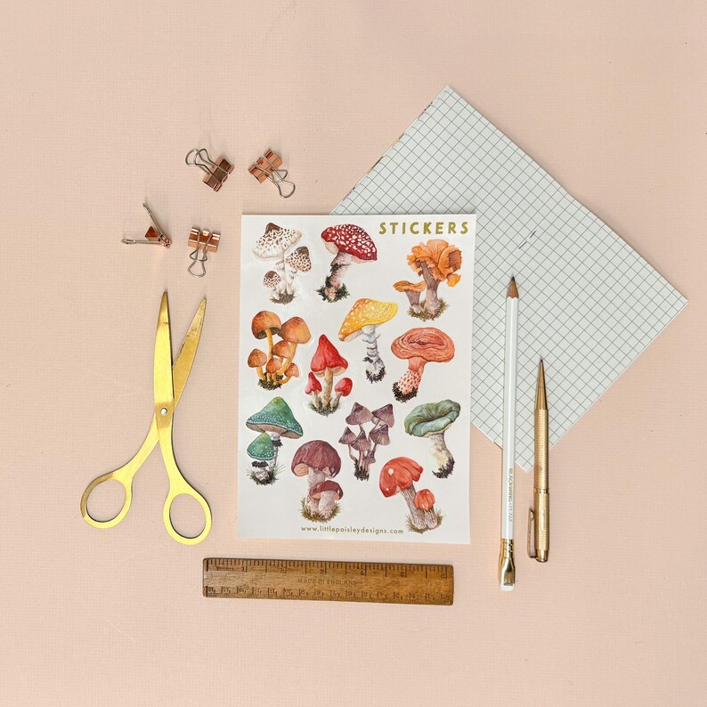 May include: A sheet of stickers featuring colorful illustrations of various mushrooms. The stickers are arranged in rows and columns on a white background. The text "STICKERS" is printed in gold lettering at the top of the sheet. The text "www.littlepaisleydesigns.com" is printed at the bottom of the sheet.