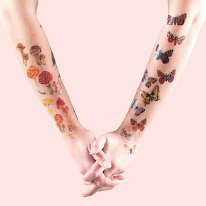 May include: Two arms with temporary tattoos of mushrooms and butterflies. The tattoos are in shades of brown, orange, red, and yellow.