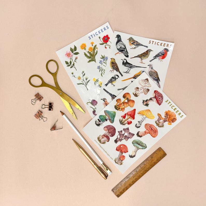 May include: Three sheets of stickers featuring illustrations of mushrooms, birds, and flowers. The stickers are on a light pink background with gold scissors, paper clips, and pencils.