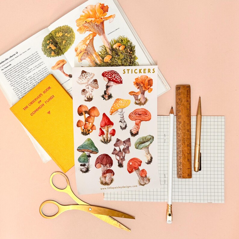 May include: A sheet of stickers featuring illustrations of various mushrooms in shades of red, orange, brown, and white. The stickers are arranged in a grid pattern and have a white background. The text "STICKERS" is printed in gold lettering at the top of the sheet. The text "www.littlepolishdesigns.com" is printed at the bottom of the sheet.