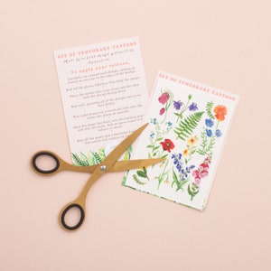 Puede incluir: Un conjunto de tatuajes temporales con dise&ntilde;os florales coloridos, incluyendo amapolas, helechos y campanillas. Los tatuajes est&aacute;n impresos en papel blanco y vienen con instrucciones sobre c&oacute;mo aplicarlos.