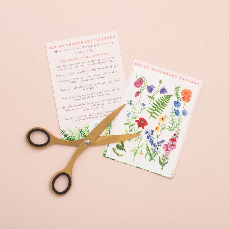 Puede incluir: Un conjunto de tatuajes temporales con dise&ntilde;os florales coloridos, incluyendo amapolas, helechos y campanillas. Los tatuajes est&aacute;n impresos en papel blanco y vienen con instrucciones sobre c&oacute;mo aplicarlos.