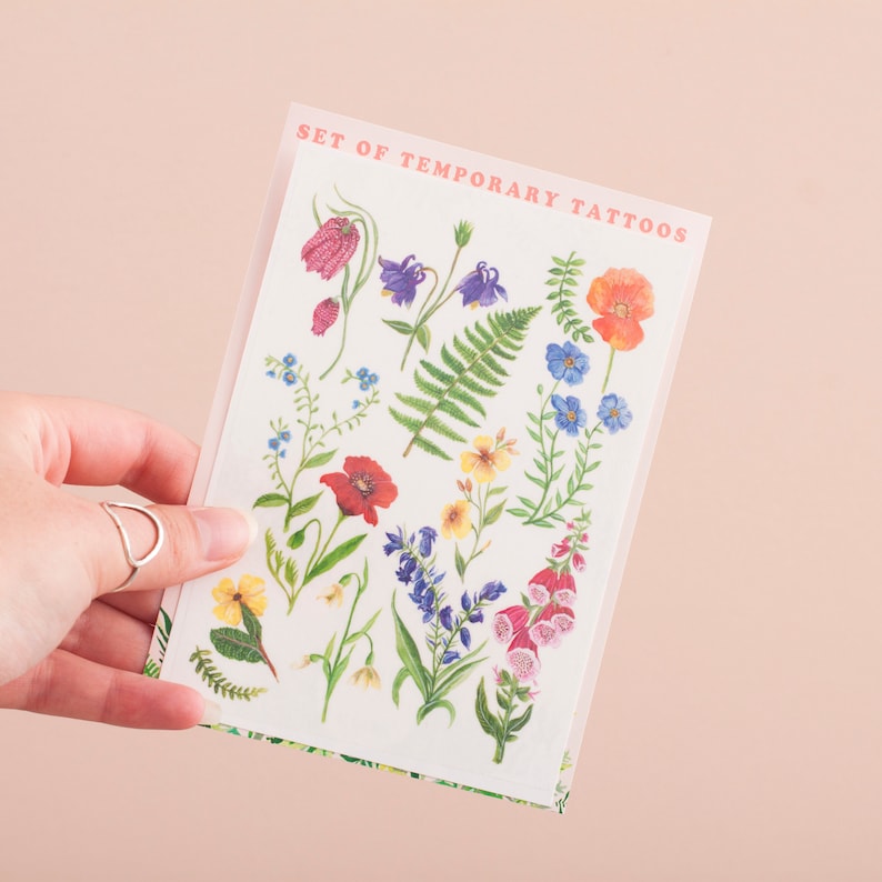 Puede incluir: Una hoja de tatuajes temporales con una variedad de flores y hojas coloridas. La hoja est&aacute; etiquetada como "Set of Temporary Tattoos".