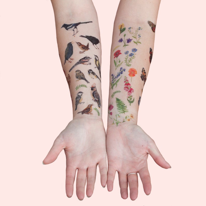 Puede incluir: Los brazos de una persona con tatuajes temporales de varias aves y flores. Los tatuajes son realistas y coloridos, y est&aacute;n dispuestos en un patr&oacute;n vertical en los brazos.