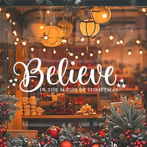 May include: A storefront window decorated for Christmas with a sign that reads "Believe in the magic of Christmas." The window is decorated with twinkling lights, greenery, and red ornaments.