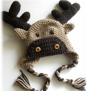 K&ouml;nnte beinhalten: Eine braune und beige gestrickte M&uuml;tzen in Form eines Elches mit einer langen, geflochtenen Schnur. Die M&uuml;tze hat zwei braune Kn&ouml;pfe f&uuml;r die Augen.