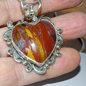 May include: A silver heart-shaped pendant with a red, yellow, and brown agate stone. The pendant has a detailed, ornate design.