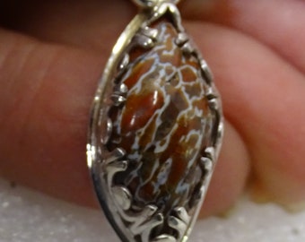 Colgante de hueso de dinosaurio petrificado, hecho a mano, engastado en bisel en plata de ley, celdas rojas, marrones y blancas.