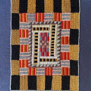 Puede incluir: Un diseño de bordado geométrico colorido con un esquema de color negro, blanco, rojo, dorado y azul. El diseño está enmarcado por un borde a cuadros dorado y negro.