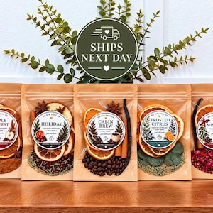 May include: Five clear stand-up pouches containing dried stovetop potpourri ingredients. Each pouch features a circular label with the names Apple Harvest, Holiday, Cabin Brew, Frosted Citrus, and Mistletoe, showcasing dried fruit, spices, and botanicals.