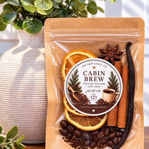 May include: A brown kraft paper pouch containing stovetop potpourri with dried orange slices, cinnamon sticks, a star anise, a vanilla bean, and coffee beans. The label reads OH SEW COZY CO CABIN BREW STOVETOP POTPOURRI COZY HOME just add water.