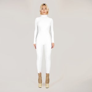May include: A white long-sleeved jumpsuit with a turtleneck. The jumpsuit is fitted and has a sleek, modern design. The model is wearing gold platform boots.