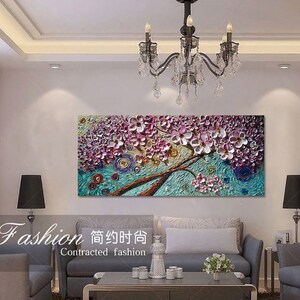 Op de afbeelding: Een kleurrijk abstract schilderij van een boom met roze en paarse bloemen. Het schilderij is ingelijst en hangt aan een witte muur in een woonkamer.