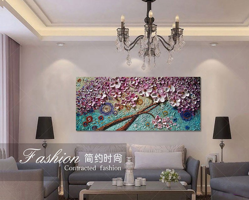 Op de afbeelding: Een kleurrijk abstract schilderij van een boom met roze en paarse bloemen. Het schilderij is ingelijst en hangt aan een witte muur in een woonkamer.