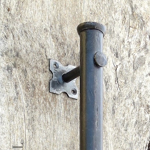 Op de afbeelding: Zwarte metalen deurgreep met een afgeronde rechthoekige vorm en twee vierkante montageplaten. De greep is gemonteerd op een licht houten oppervlak.