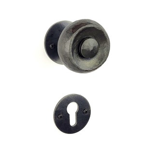 May include: A black metal door knob with a round, textured design. The knob has a keyhole cover and is attached to a round base plate.