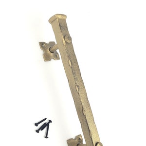 May include: Gold-toned metal door pull handle with a square design. The handle has a textured surface and is mounted on a wall with two square plates. The handle is approximately 30 cm long.