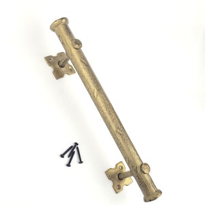 May include: Gold metal handrail with a decorative design. The handrail is attached to a wall with two square brackets and screws. The handrail is approximately 45 cm long.