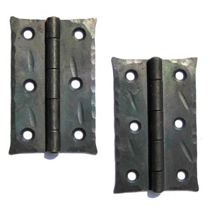 May include: Two black metal hinges with a decorative hammered finish. Each hinge has four holes and a barrel-shaped pin.