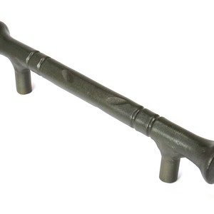 May include: A dark gray metal cabinet pull with a textured finish and a slightly curved design. The pull has a rounded end on each side.