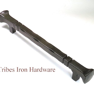 Könnte beinhalten: Ein schwarzer Türgriff aus Metall mit gehämmerter Oberfläche und quadratischen Akzenten. Der Griff ist etwa 20 cm lang. Tribes Iron Hardware ist unter dem Griff aufgedruckt.