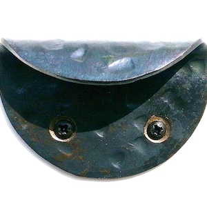 Könnte beinhalten: Ein halbrundes, dunkelblaues Metallgriff mit zwei Schrauben. Der Griff hat eine gehämmerte Textur und eine leicht gebogene Form.