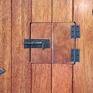 Puede incluir: Una puerta de madera con un peque&ntilde;o panel de puerta con bisagras. El panel tiene un pestillo de metal y dos bisagras. La puerta est&aacute; hecha de tablones de madera.
