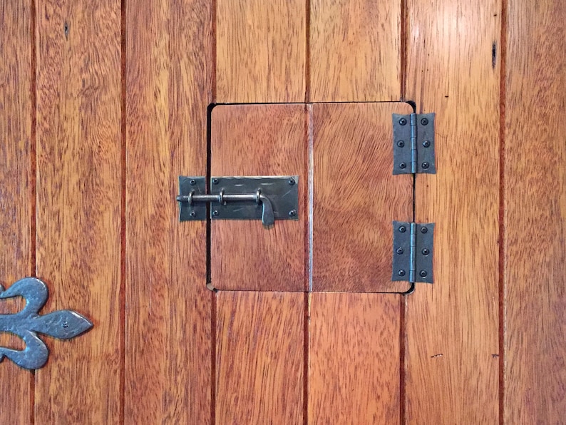 Puede incluir: Una puerta de madera con un peque&ntilde;o panel de puerta con bisagras. El panel tiene un pestillo de metal y dos bisagras. La puerta est&aacute; hecha de tablones de madera.