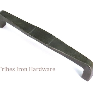 May include: A dark gray metal cabinet pull with a rectangular shape and a slightly curved design. The pull has a textured surface and a slightly raised edge.