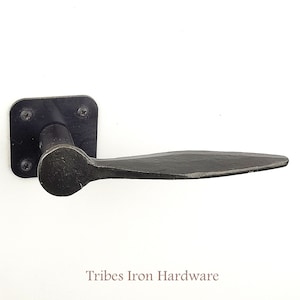 Può includere: Maniglia per porta in metallo nero con una piastra posteriore quadrata e una leva lunga e piatta. Tribes Iron Hardware è stampato sotto la maniglia.