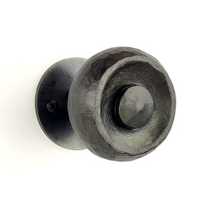 Può includere: Una maniglia per porta in metallo nero con un design rotondo e testurizzato. La maniglia ha un'area rotonda più piccola e incassata al centro.