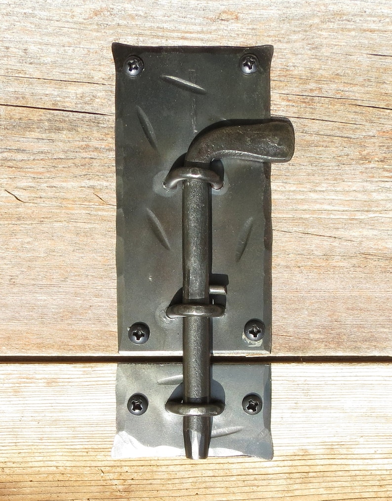 Puede incluir: Pestillo de puerta de metal negro con una superficie texturizada y un mango curvo. El pestillo est&aacute; fijado a una superficie de madera con tornillos.