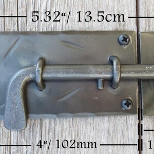 Puede incluir: Pestillo de puerta de metal negro con un pestillo en forma de L de 102 mm de largo. El pestillo mide 13,5 cm de ancho y 5,3 cm de alto.