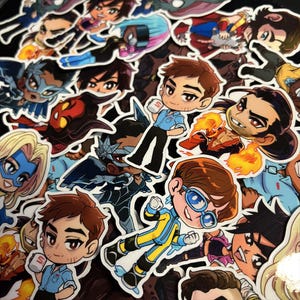 May include: A collection of colorful cartoon stickers featuring various characters in action poses. The stickers showcase a variety of designs, including superheroes and other stylized figures. The stickers are on a black background.