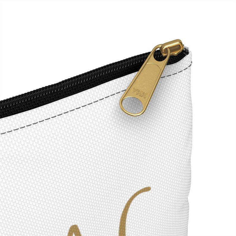 May include: White zippered pouch with a black zipper and a gold YKK zipper pull. The pouch has a gold design on the front.