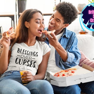 May include: A couple enjoys pizza together on a couch. The woman is wearing a white t-shirt with the text "Blessings Over Curses" printed on it.