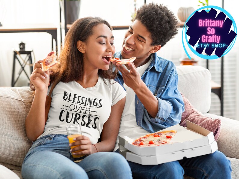 May include: A couple enjoys pizza together on a couch. The woman is wearing a white t-shirt with the text "Blessings Over Curses" printed on it.