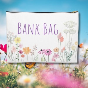 May include: White zippered pouch with the text "BANK BAG" in purple lettering. The pouch is decorated with a watercolour floral design of pink, yellow, and green flowers.