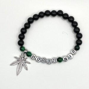 May include: Black and green beaded bracelet with a silver charm of a marijuana leaf and the word "HUMAN" spelled out in silver beads.
