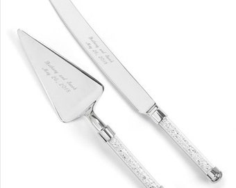 May include: A silver cake knife and server set with crystal-embellished handles. The knife has the inscription "Brittany and David May 26, 2015" and the server has the inscription "Brittany and David May 26, 2015".