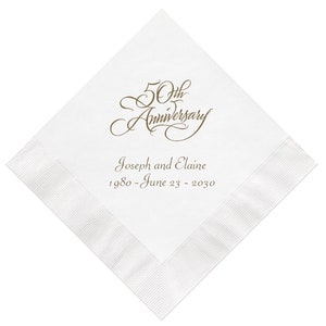 May include: A square white paper napkin with a textured border. The center features gold script text reading 50th Anniversary, followed by the names Joseph and Elaine and the date range 1980 - June 23 - 2030 printed in a simple font.