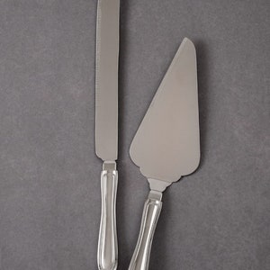May include: A set of two silver cake servers. The larger server has a scalloped edge and the smaller server has a serrated edge.