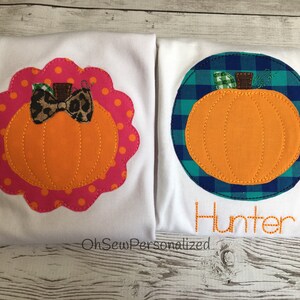 May include: Two white t-shirts with pumpkin appliqu&eacute;s. One has an orange pumpkin with a leopard print bow on a pink polka dot scalloped border. The other has an orange pumpkin on a blue and green plaid circle with the name "Hunter" stitched below.